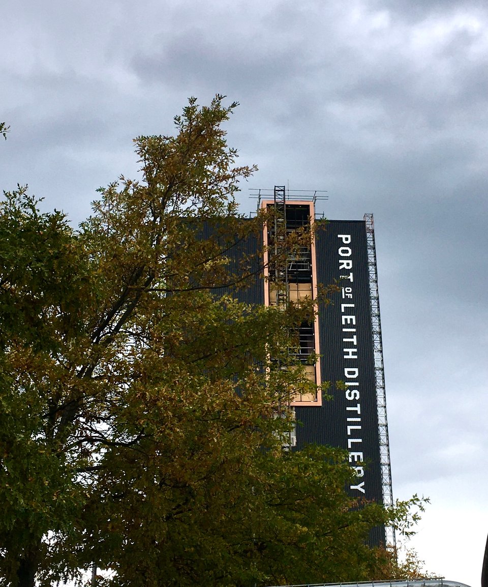 Port of Leith whisky distillery behind a tree starting to turn from green to gold, and against a grey and cloudy Edinburgh sky. Image by Rowan Ambrose.