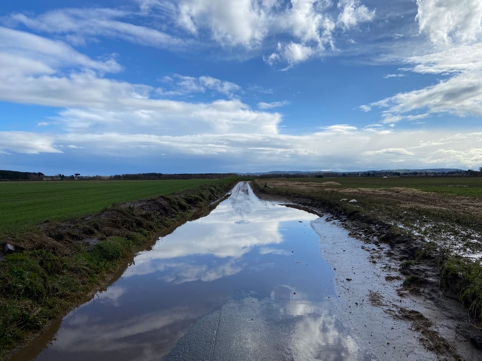 A road with a huge puddle covering the whole thing and reflecting the blue sky above