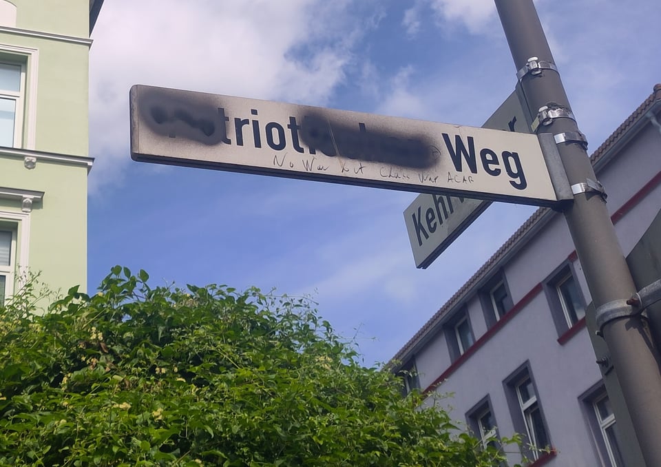 Straßenschild, das mit schwarzer Farbe so verschmiert ist, dass nur noch "riot Weg" zu lesen ist