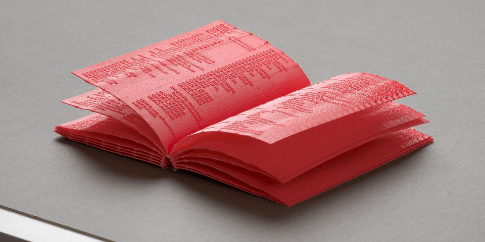 A photo of a book that is made of what appears to be red rubber or plastic -- each page is that material, and the words on the page are raised letters of that material.