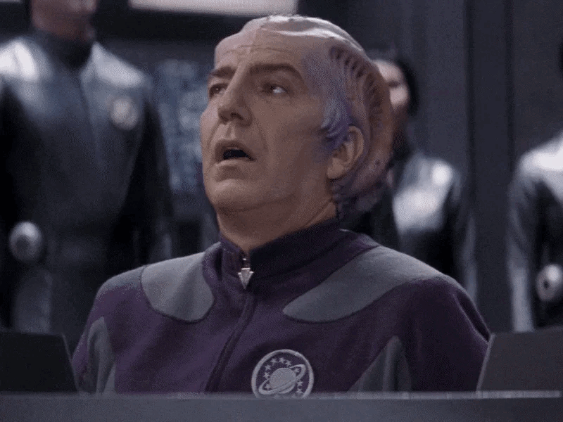 Sir Alexander Dane, Alan Rickman’s character from Galaxy Quest,  sighs in relief and slumps in his chair as a crowd of Thermians applaud him.