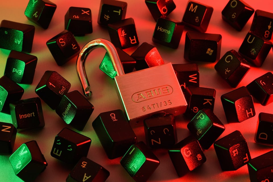 An image of an open padlock, surrounded by computer keyboard keys. The scene is cast in a reddish light. Photo by FLY:D on Unsplash