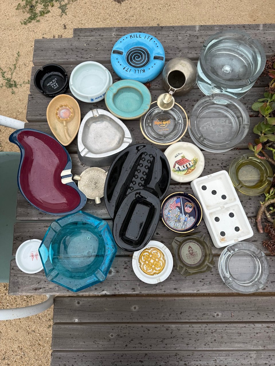 A wooden picnic table with a variety of unusual multicolored ashtrays. It was drizzling, so there are little spots on the table.