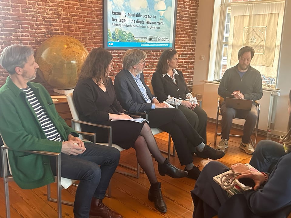 Five people sit in chairs in front of a room - they all look at the moderator who is reading off his laptop.