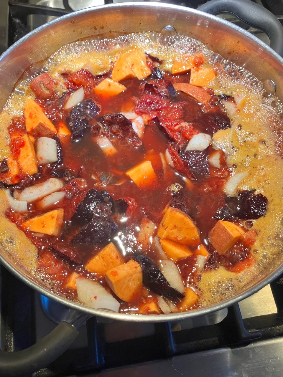 A boiling pot filled with chunks of plums, orange sweet potato, and white onion.