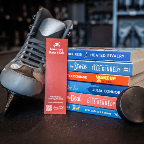 An ice skate leaning against a pile of hockey romance novels, with a Lovestruck bookmark propped in front.