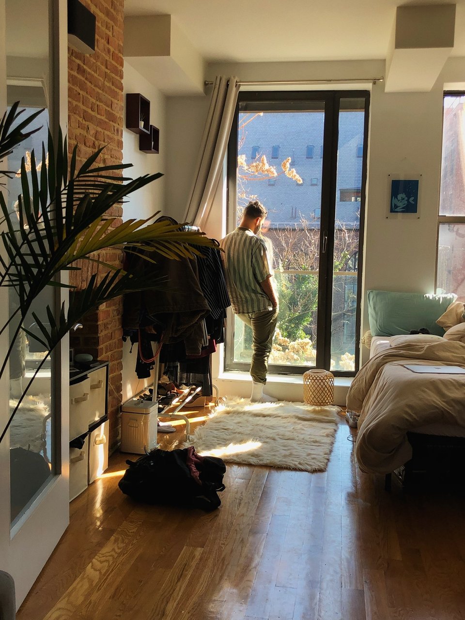 Yatú standing before the glass door of an apartment looking out of it. Soft light is coming in through the window and the apartment looks serene and calm.