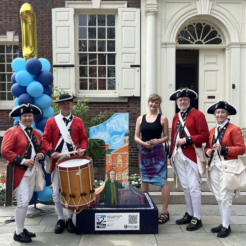 photo of a fife and drum company with a piece of public art and the painter who created it