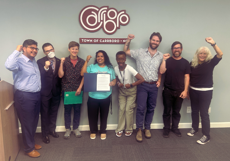 The Mayor and other Members of the Carrboro Town Council raise fists and pose with two representatives from Siembra NC after reading the 4th Amendment Workplace proclamation on 20th May 2025 4th_workplace.png