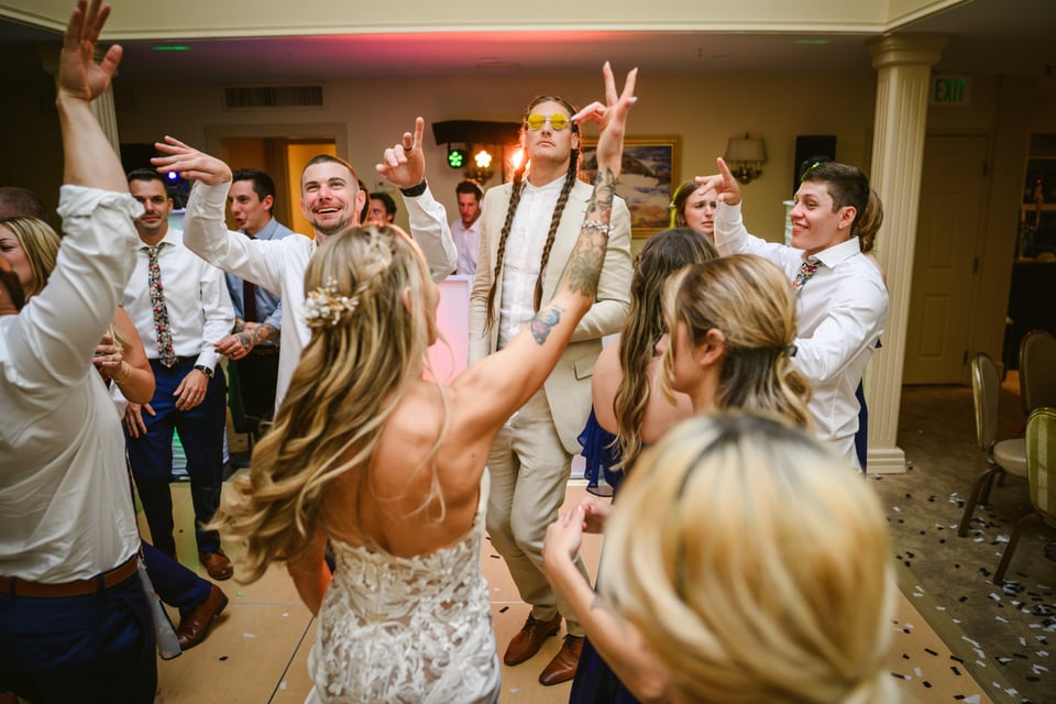 Wedding party dancing on the dance floor. A very tall man is in the middle with stylish sunglasses and braids