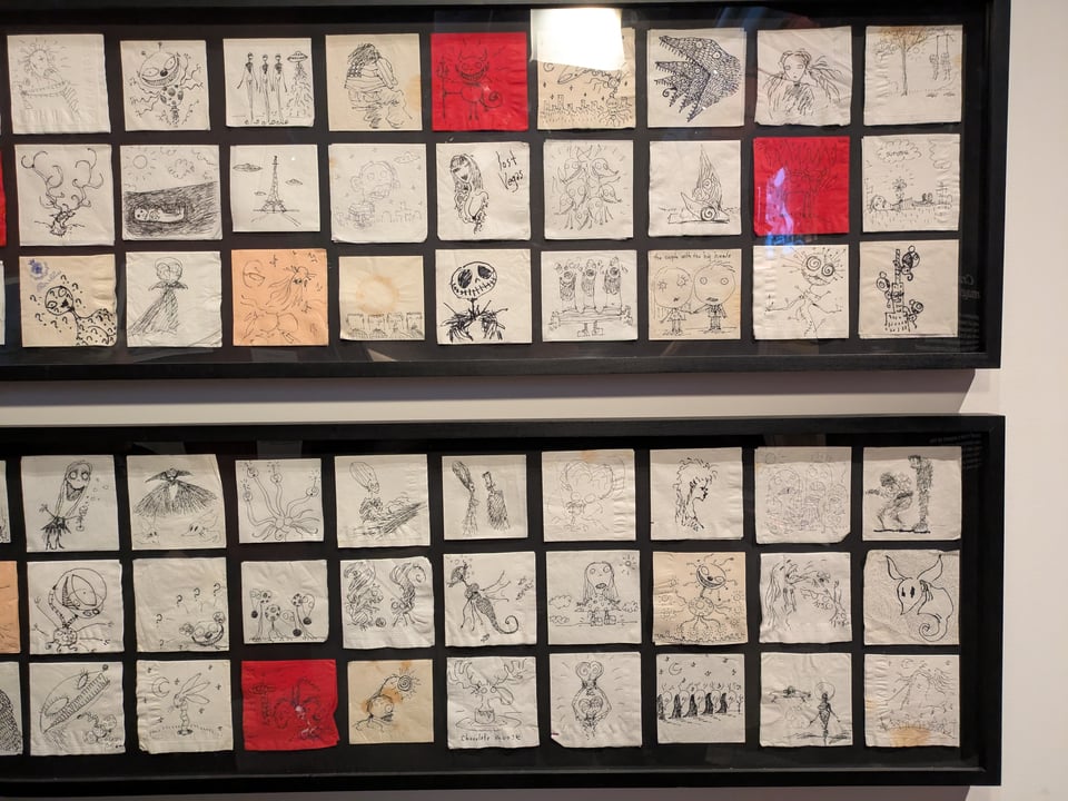 Two long picture frames full of various napkin sketches from Tim Burton
