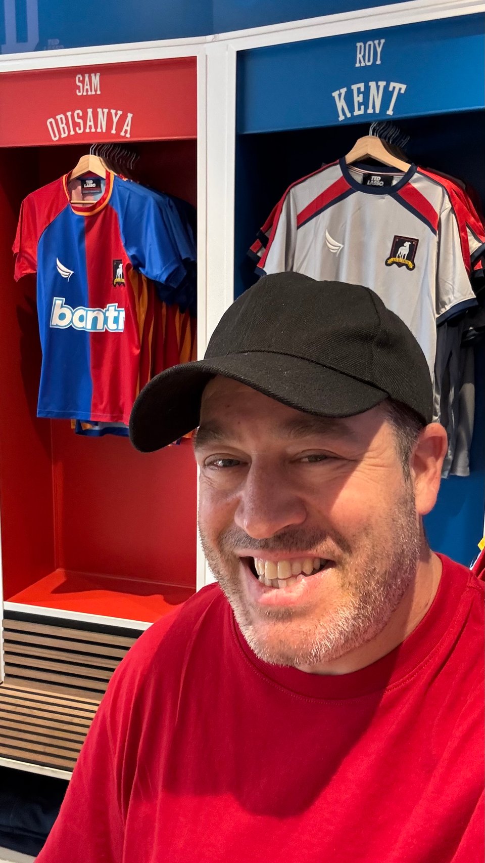 Neil in the Ted Lasso store in Richmond, London, standing in front of lockers for Sam Obisanya and Roy Kent