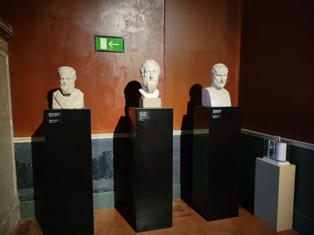 Three busts of ancient Greek men, on shoulder-high black pedestals.