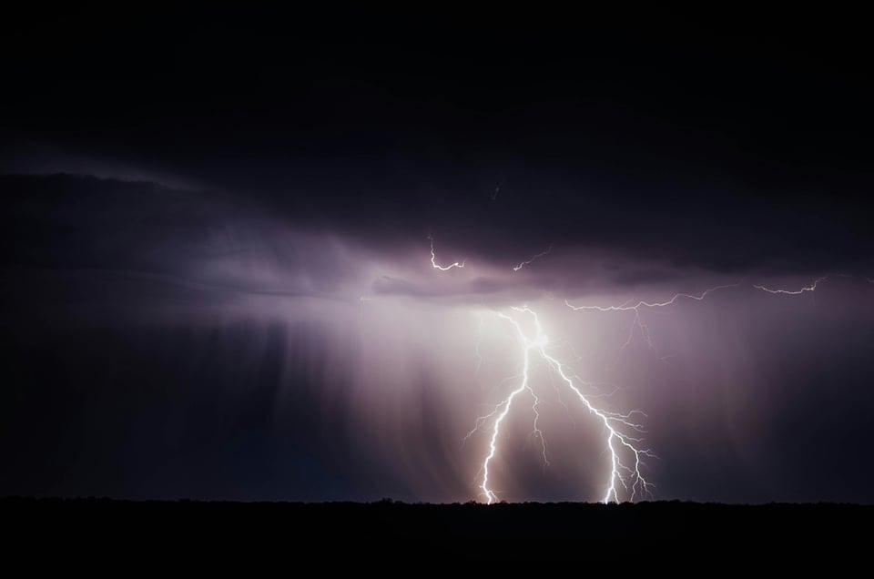 A dark purple storm in which two forks of lightning look like bright spindly legs walking across the landscape.