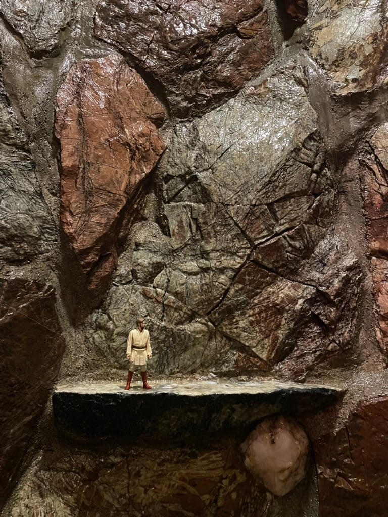 A wall of glistening rock. On a ledge there is a small action figure of Obi-Wan Kenobi