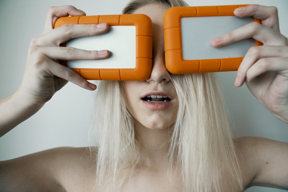 A woman holding two external hard drives over her eyes. Photo by JC Gellidon on Unsplash