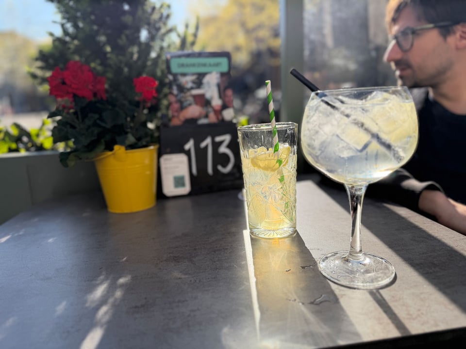 A restaurant table with two mocktails in the sunlight with a profile of a man in the background.
