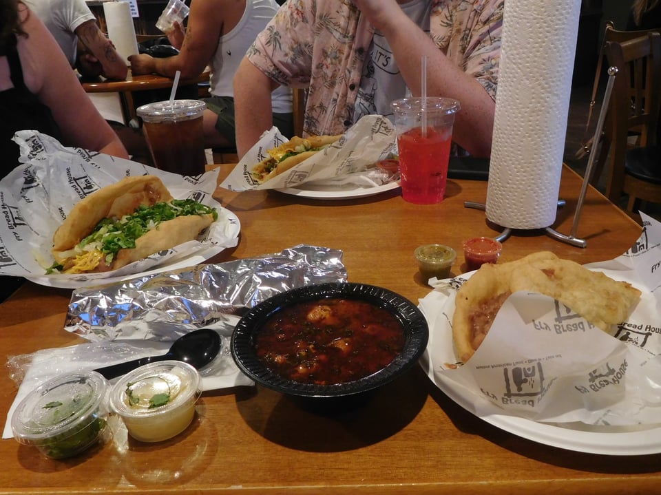 A table with several paper plates of fry bread and a bowl of meaty-looking stew
