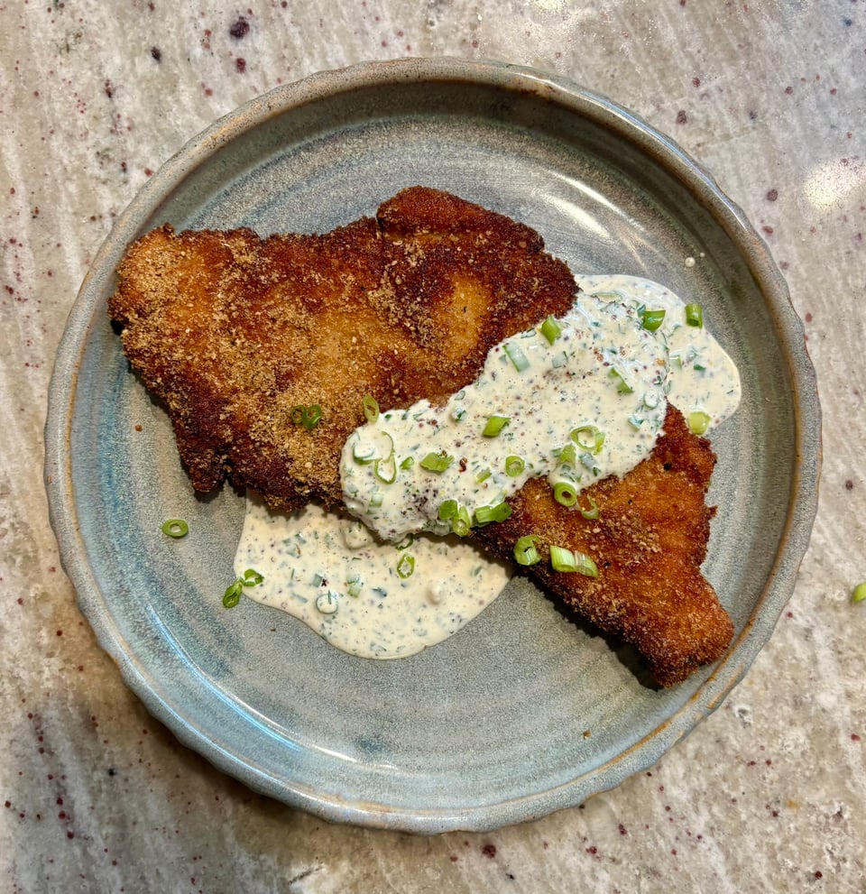 A fried porkchop smothered in a Chinese rang and scallions on an earth-toned plate.