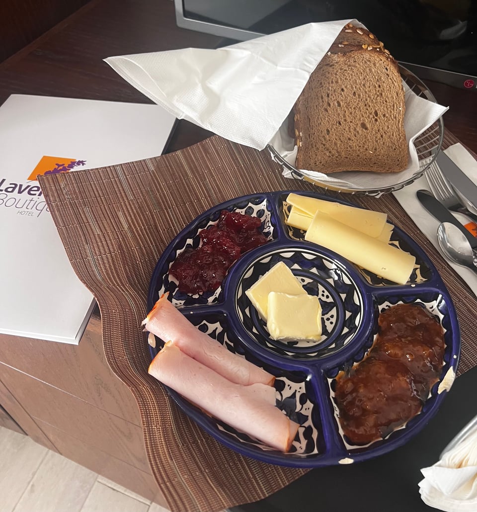 A blue and white platter holding cheese, turkey slices, butter, and two kinds of jam