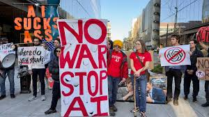image of protestors holding signs that say "AI sucks ass" and "No war stop AI."