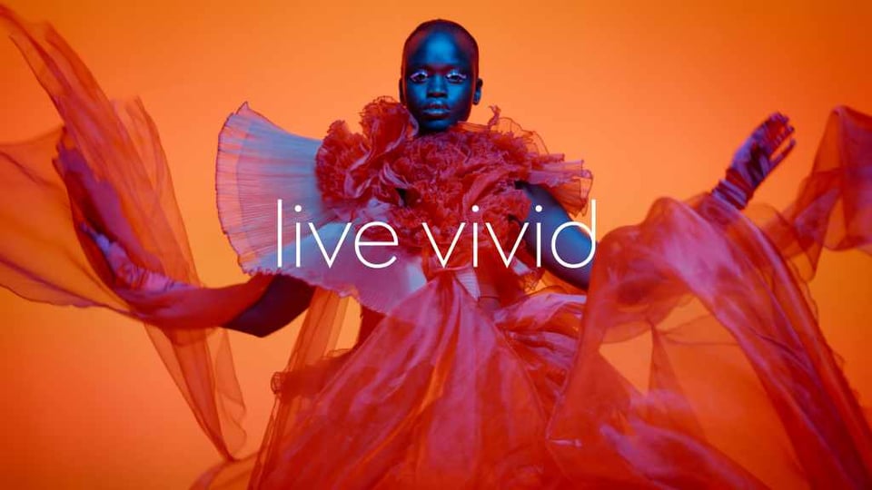 one of the more striking shots from Jaguar's campaign with a dark-skinned black model illuminated in neon blue, surrounded by floating waves of glowing red fabric in a way that strongly evokes the way air moves over a vehicle in motion. it's captioned 'live vivid'
