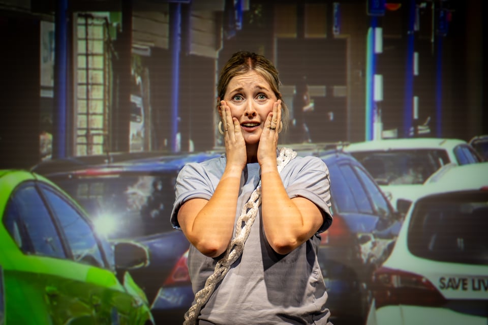 Lesa in front of a busy Newtown street, both hands on her cheek, looking shocked right before saying 'mamma mia!'