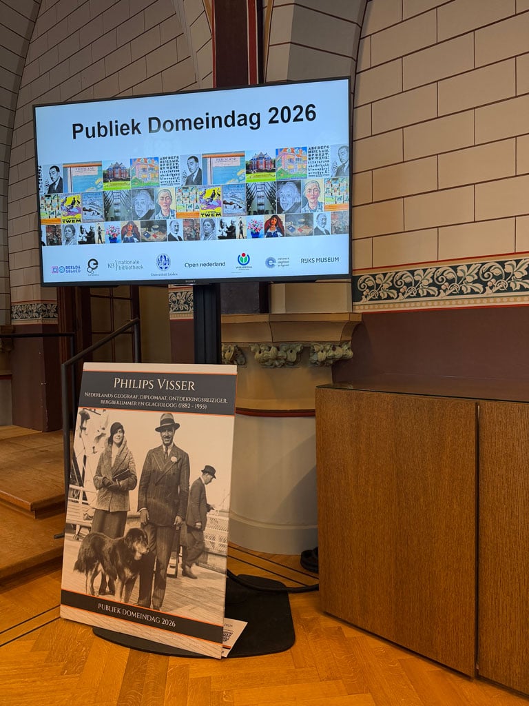 A screen shows a collage of people and artwork that is now in the public domain in Europe. Underneath the screen, there is a poster board with a photo of Philips Visser and his wife and their dog.