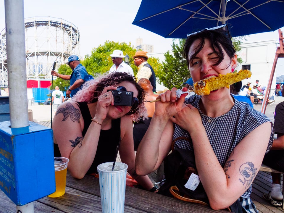 grace snapping a photo and erin taking a big bite of street corn.