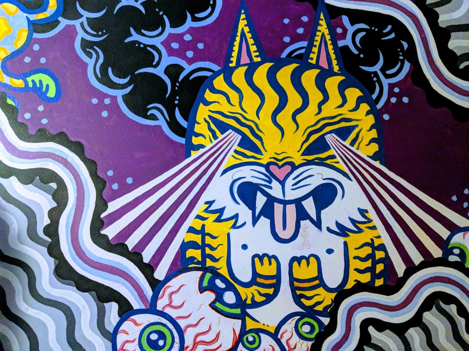 Street art of a tiger-striped cat shooting beams out of its eyes into clouds and eyeballs.