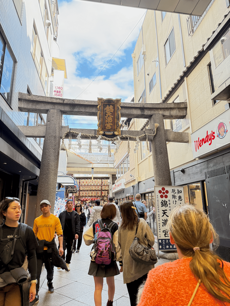 a group of people walking down a narrow shopping street in Kansai.