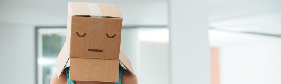 A person with a box on their head. There's a sad face drawn on the box.