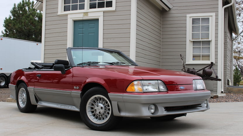 A picture of a maroon 1987 convertible mustang car.