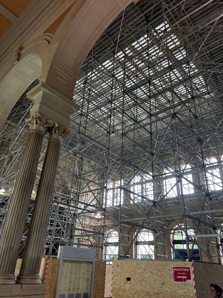A mid-nineteenth-century train station hall filled with light scaffolding up to a skylit ceiling