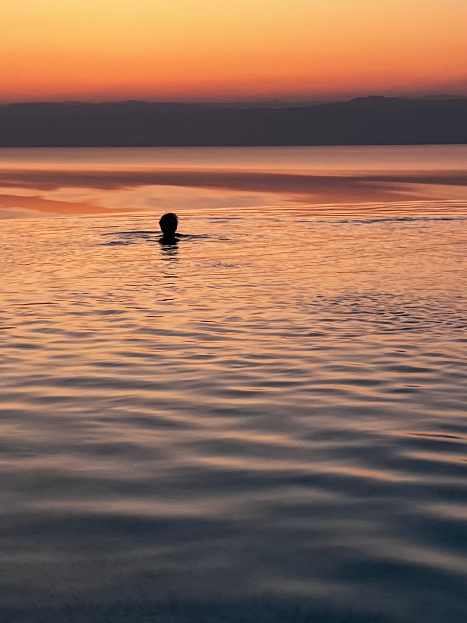 A person's head that is in complete shadow, against a background of water glowing orange (after the sun has just set))