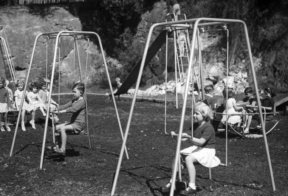 A black and white photo of children in 1950 playing on vintage playground equipment.