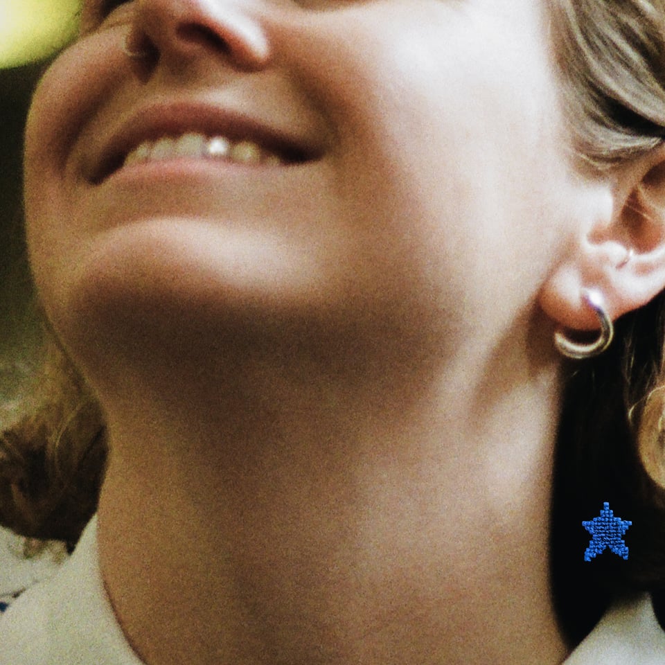 A close-up of a smiling person's face with a focus on their neck and earrings, one featuring a blue star design.