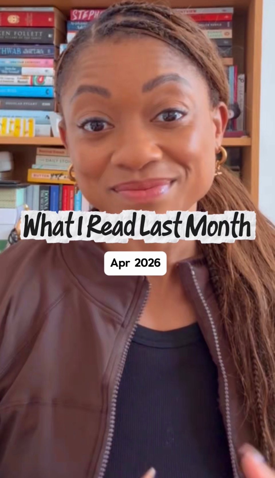 Portrait-style video screenshot of Nadia smiling at the camera in front of bookshelves. Overlaid text reads: “What I Read Last Month” with a smaller label underneath saying “Apr 2026.” She is wearing a brown sports jacket over a black top.