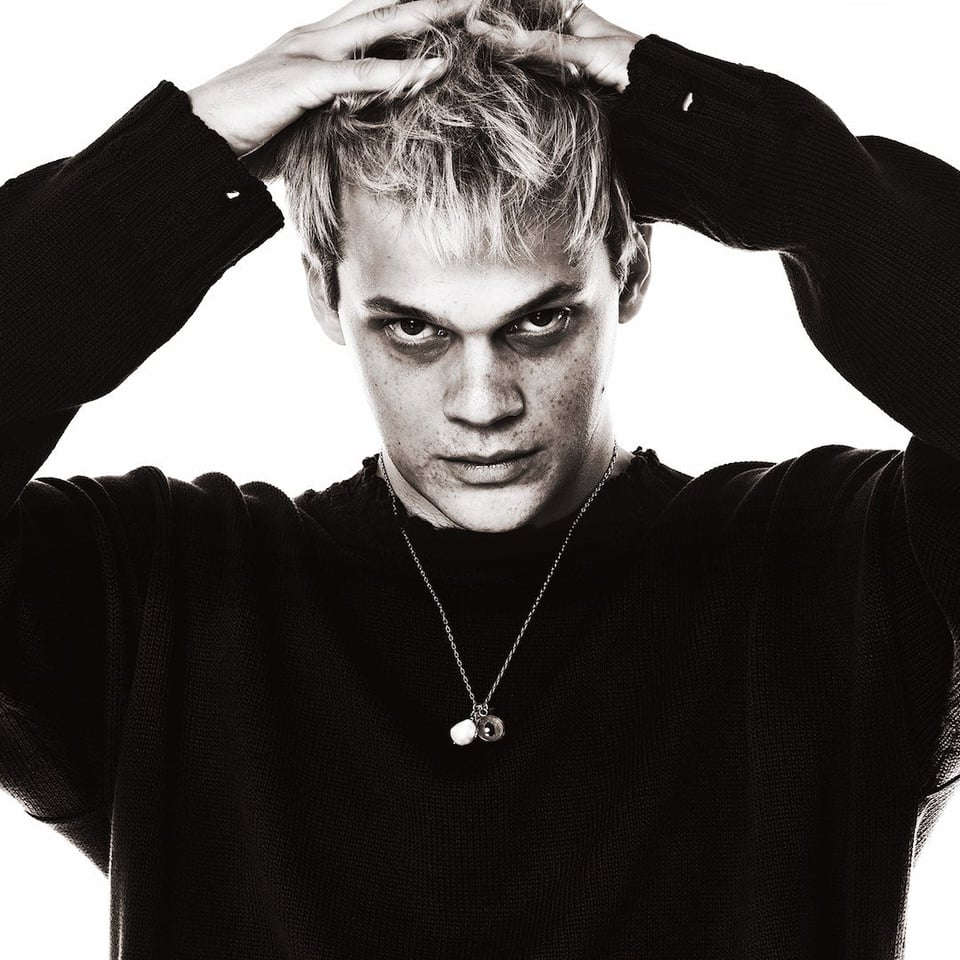 A black and white photo of George Clanton in a black sweater with his hands on his head.