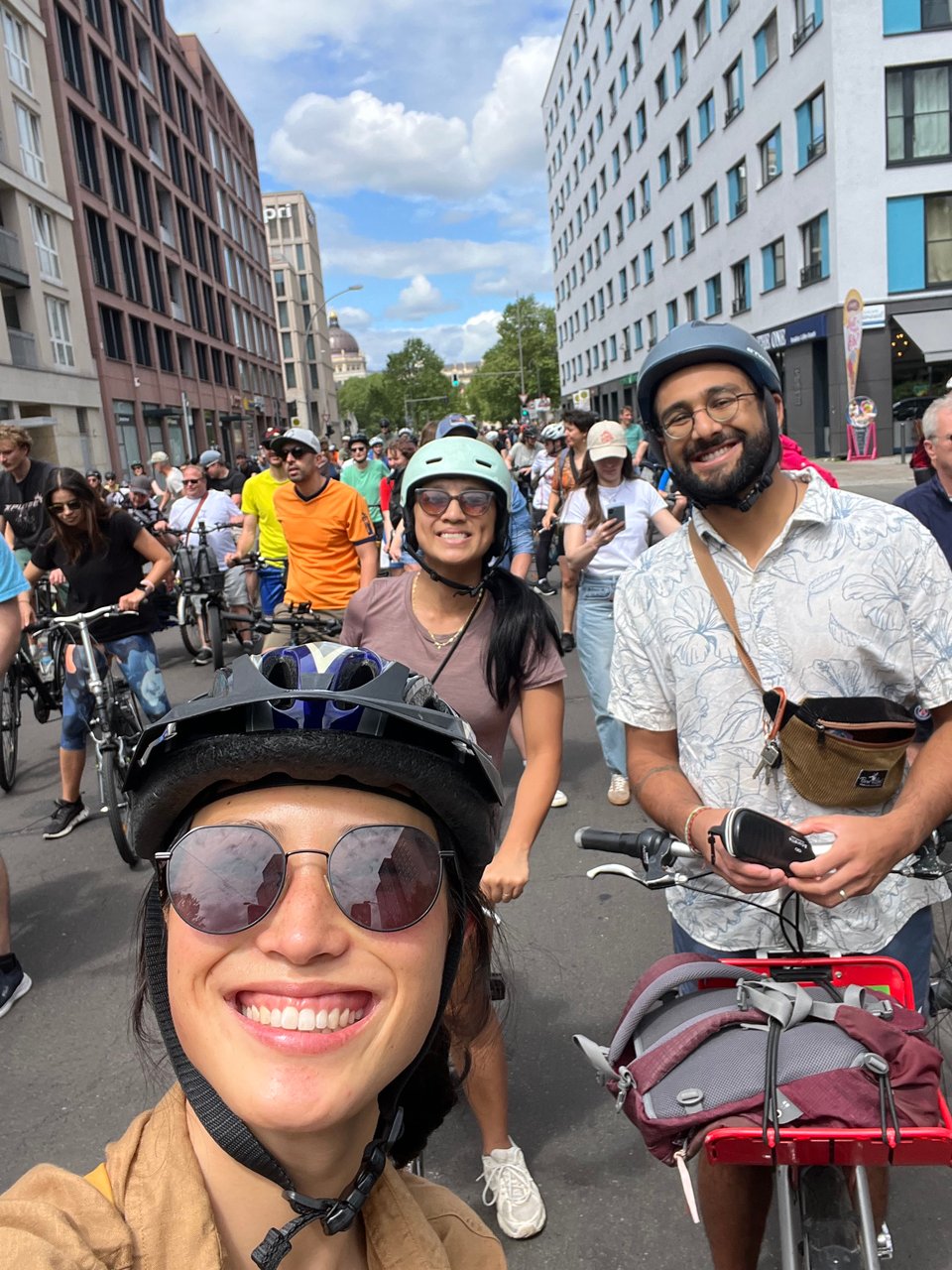 Three people on bicycles smiling in a selfie, among a huge crowd of cyclists