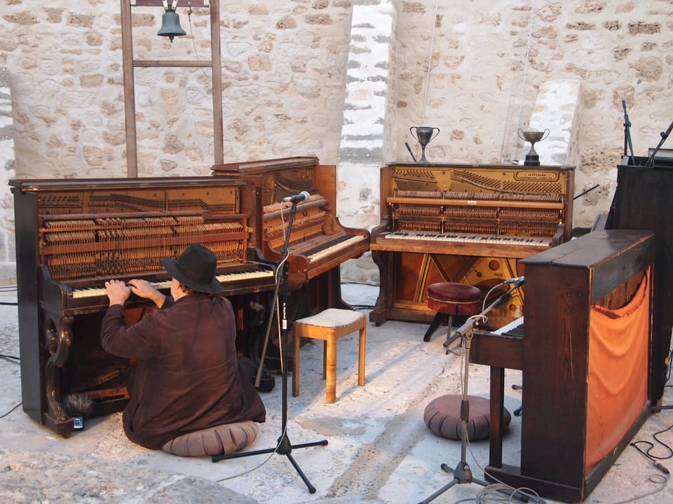 Ross Bolleter performing with fived ruined pianos arranged in a semi-circle