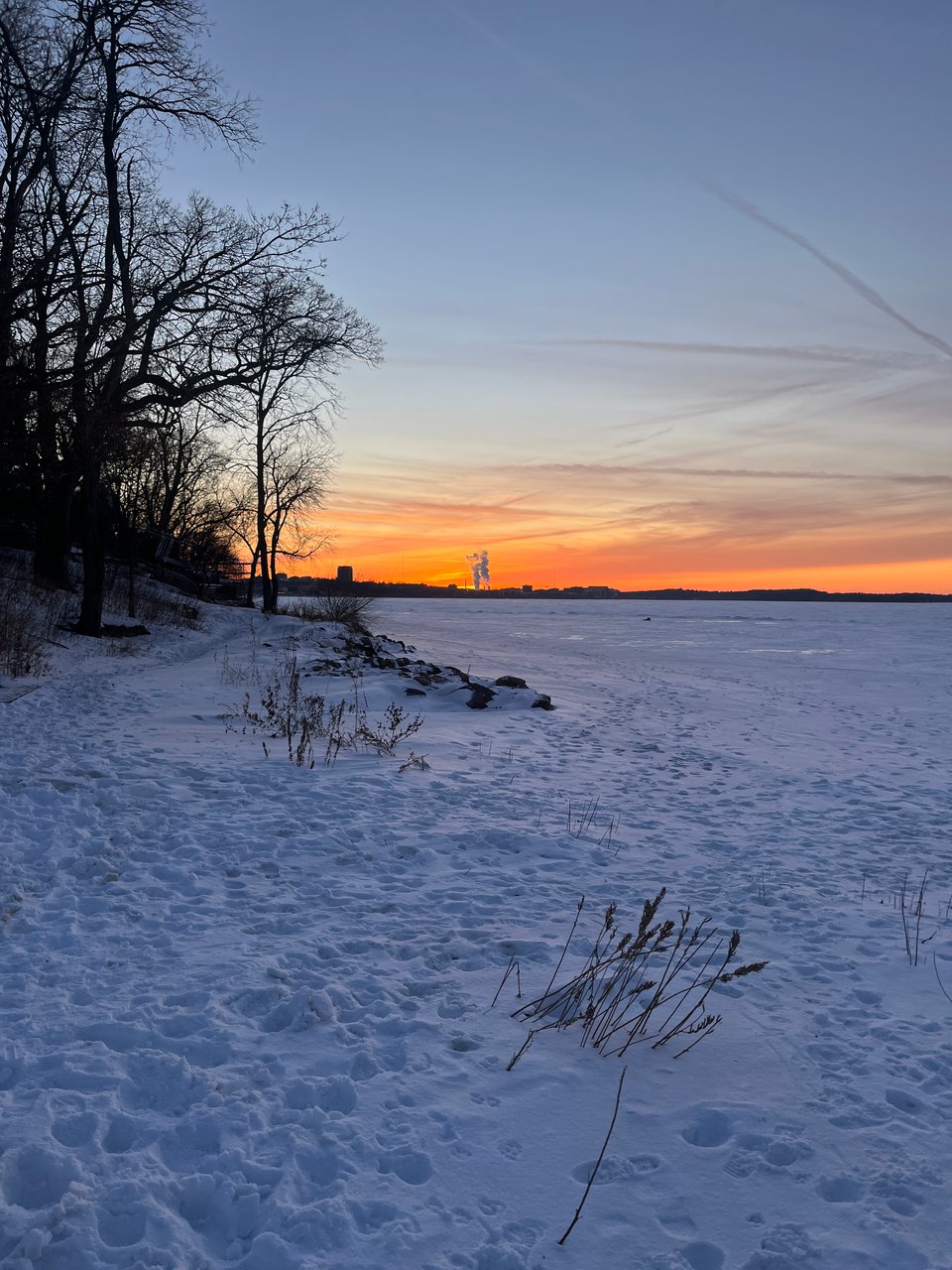 orange wispy sunset along snow-covered lakeshore full of footprints