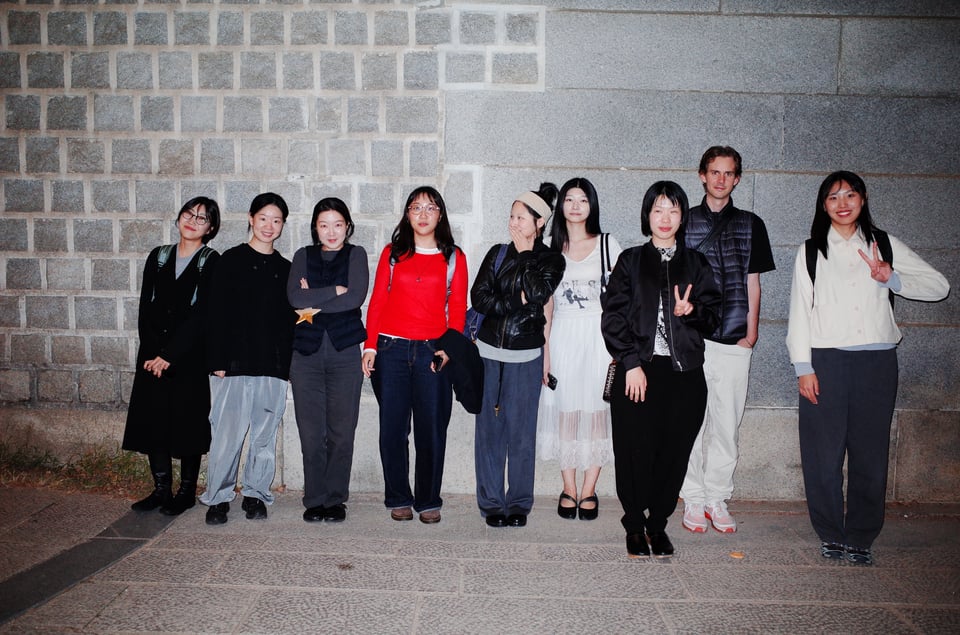 A group of people stand in a line alongside a cinderblock wall. A cute image.