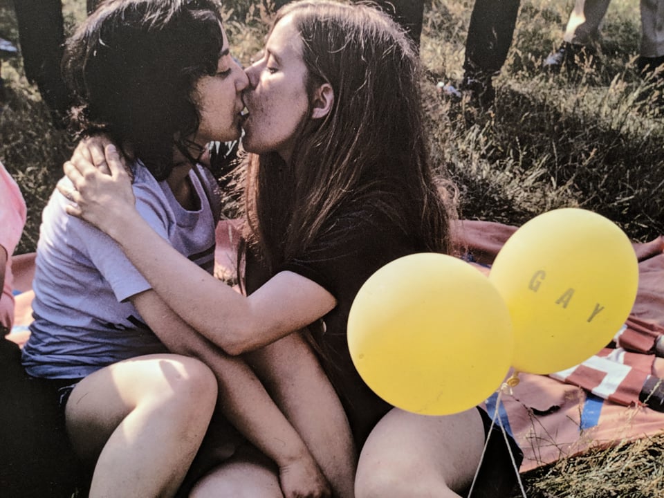 Two young women kissing, holding yellow balloons that say GAY