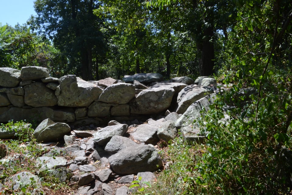 A somewhat tumbledown wall built of large stones, surrounded by trees.