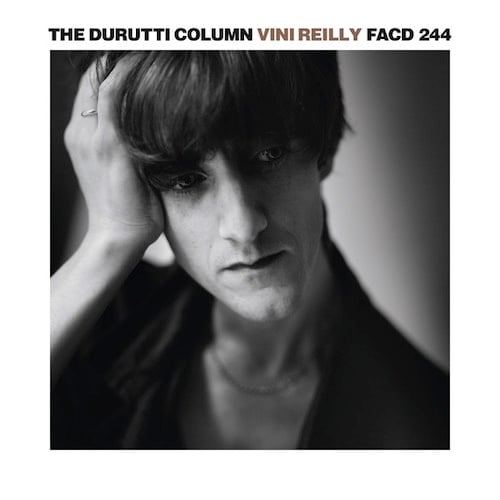 A sharp, well-executed black and white photograph of The Durutti Column's Vini Reilly (yes he named the album after himself.) The photo is a close-up, from the shoulders up. Reilly has a very long thin angular face, with long thick brown bangs crowning his head. He has thin lips and a cleft chin. He looks to the right with his hand holding up his head. He has a thoughtful look on his face.