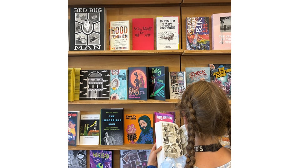 A shelf filled with self published zines with a young girl in braids in the front.