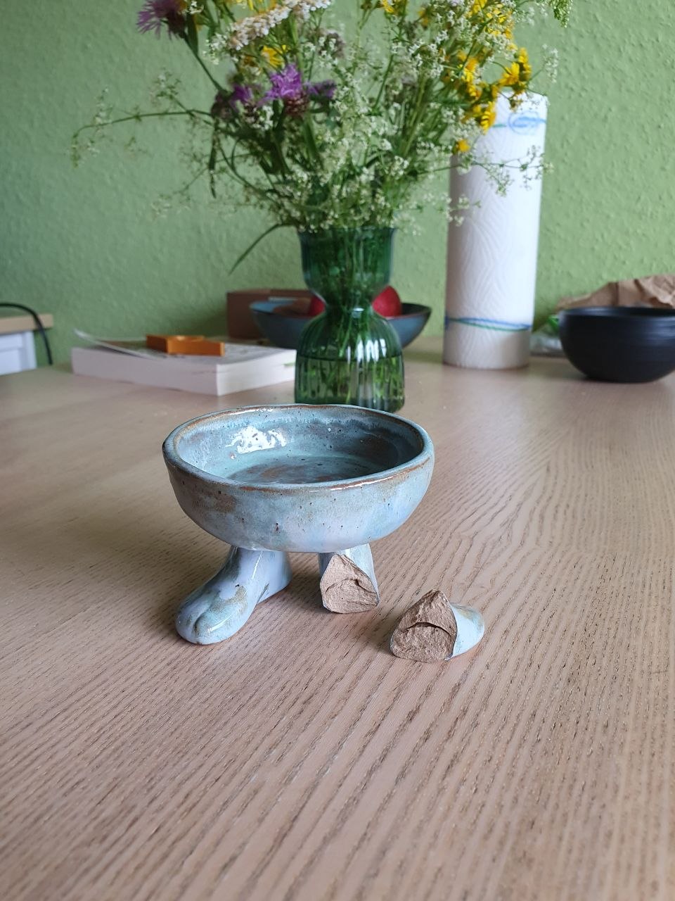 A photo of a blue-glazed footed bowl. One foot is broken off and the broken bit is next to the bowl.