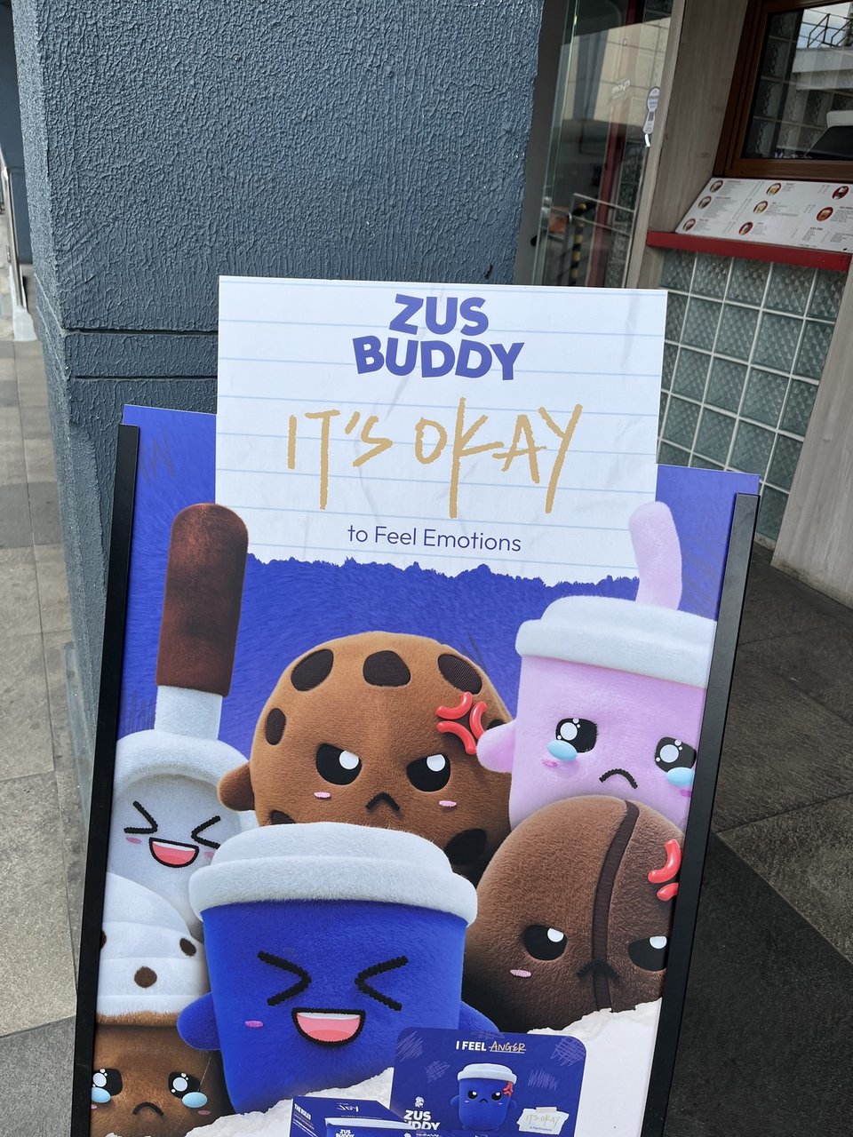 a sandwich board showing stuffed coffee beans and cups with varying emotions and the words "it's okay to feel emotions"