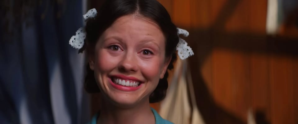 A still from the ending of the movie Pearl (2022) featuring Mia Goth smiling at the camera.